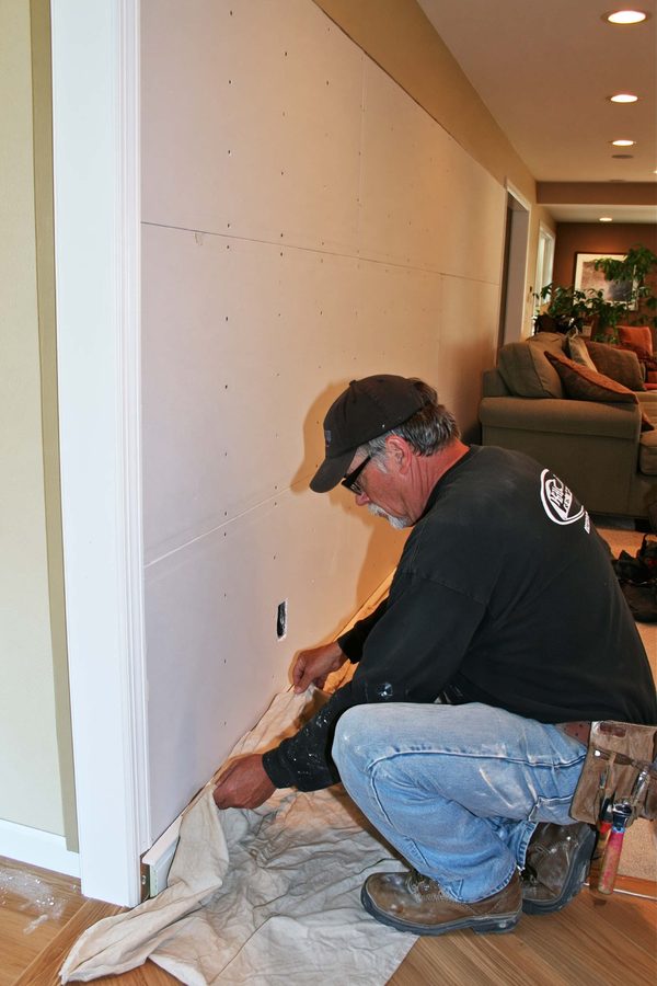 Contractor arranging a drop cloth beneath newly installed drywall.