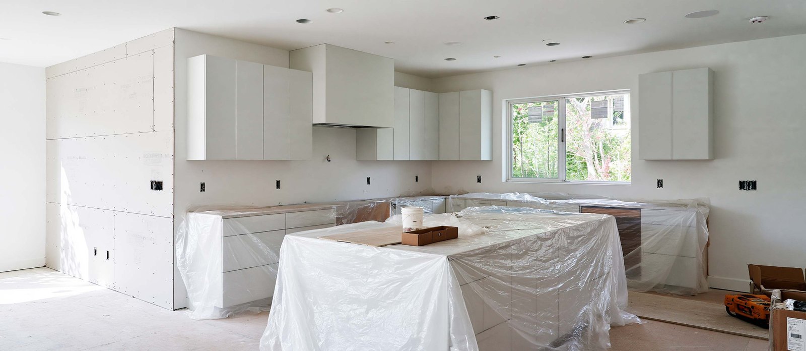 New drywall surrounding a kitchen with cabinets and counters covered for the work.