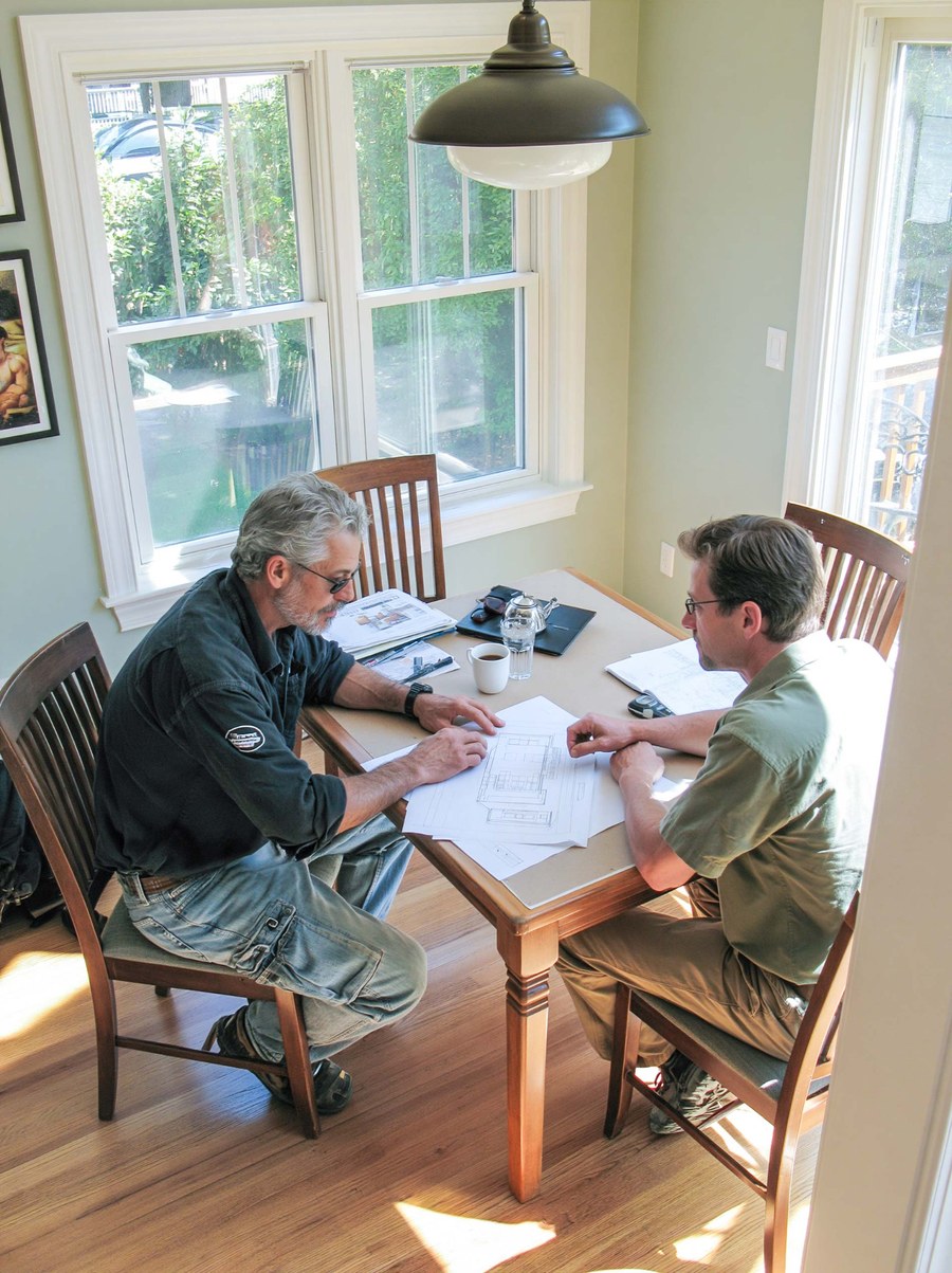 Two people reviewing house plans at a dining table.
