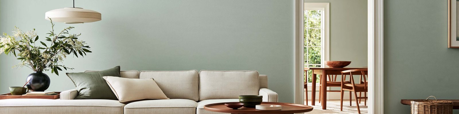 Sage living-room walls behind a sofa and a doorway into a dining room.