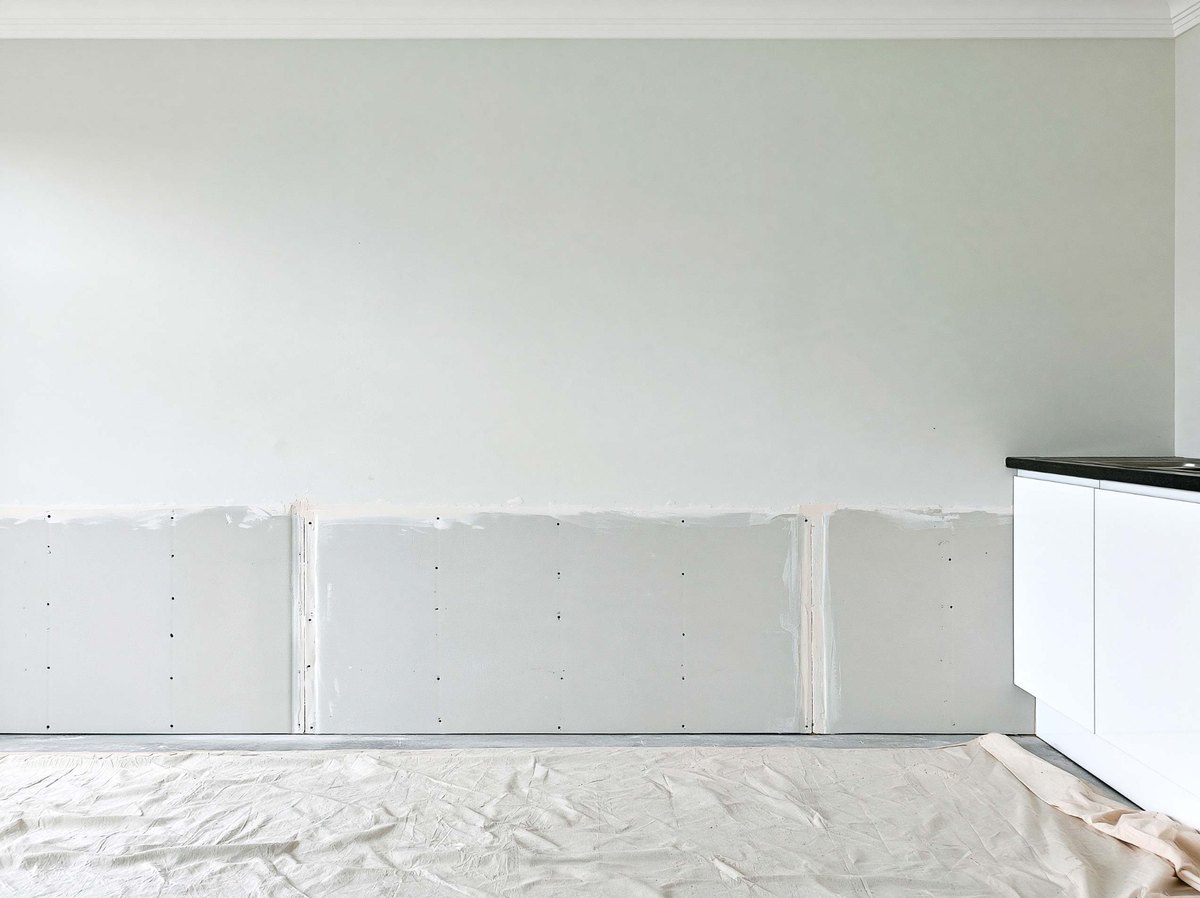Replacement drywall fitted along the lower portion of a room wall.